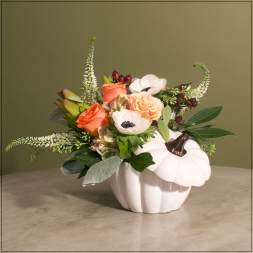 Orange roses and white anemones arranged in a white pumpkin vase