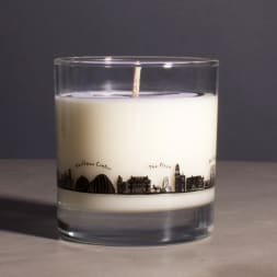 White candle in a clear glass tumbler with a city skyline design