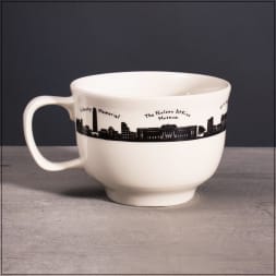 White ceramic mug with a black city skyline and labeled landmarks around the rim.