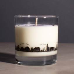 White candle in a clear glass tumbler with a city skyline design