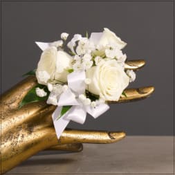 White rose corsage with baby's breath and ribbon on a gold hand display