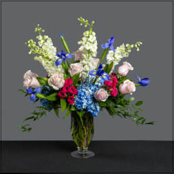 Mixed bouquet of roses, hydrangeas, and blue irises in a glass vase