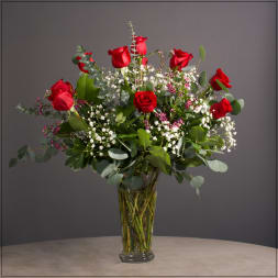 Red roses arranged in a clear glass vase with white filler flowers