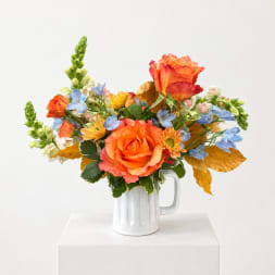 Orange and blue mixed bouquet in a white mug vase