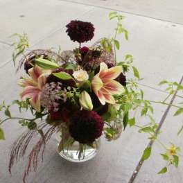 Low glass vase with burgundy dahlias and pink lilies with trailing greenery.