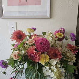 Loose garden-style arrangement of pink dahlias, roses, and white hydrangeas in a clear glass vase