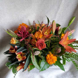 Low arrangement of orange lilies, roses, marigolds, orchids and mixed blooms in warm autumn tones