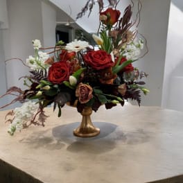 Red rose arrangement in a gold pedestal vase with white blooms