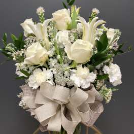 White roses and lilies in a glass vase with a large beige bow
