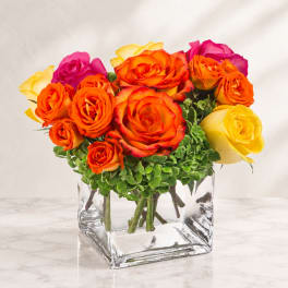 Bouquet of orange, yellow, and pink roses in a clear square vase