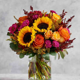 Bouquet of sunflowers and orange roses in a clear glass vase
