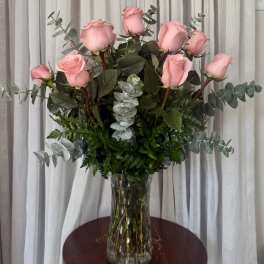 Pink roses arranged in a clear glass vase with eucalyptus foliage