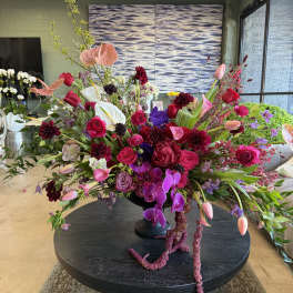 Large asymmetrical arrangement of pink, red, purple, and white flowers in a black pedestal vase on a round table