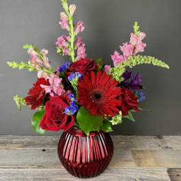 Red roses and gerbera daisies in a ribbed red glass vase