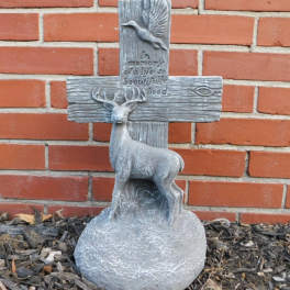 Gray memorial cross with a deer and bird relief against a brick wall
