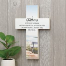Cross-shaped memorial plaque with a Father’s tribute and a potted plant beside it