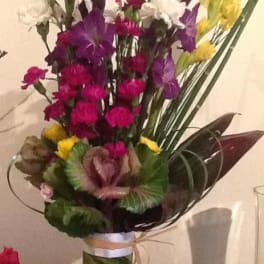 Tall mixed bouquet in a striped vase with pink, purple, white, and yellow flowers.