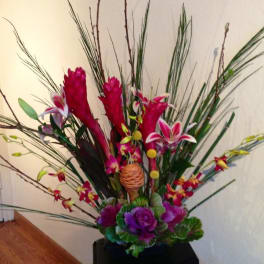 Tall tropical floral arrangement with pink and purple blooms in a black container