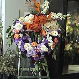 Heart-shaped floral wreath with white, purple, and orange flowers on an easel