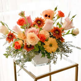 Mixed bouquet of peach, coral, and white flowers in a clear glass vase