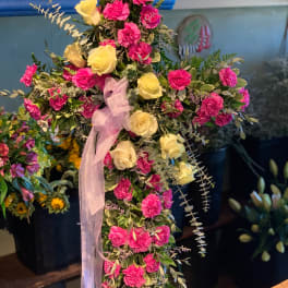 Standing cross spray of hot pink carnations and pale yellow roses with a sheer ribbon bow.