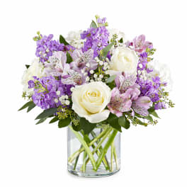 Round arrangement of white roses and purple flowers in a clear glass vase