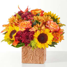 Autumn bouquet with sunflowers, roses, and mums in a leaf-patterned vase
