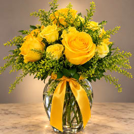 Yellow roses in a clear glass vase with a yellow ribbon