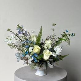 Loose bouquet of pale roses, white blooms, and blue accents in a light blue vase