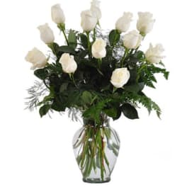 White roses arranged in a clear glass vase with greenery
