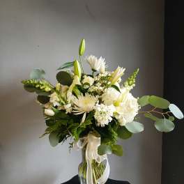 White floral arrangement in a clear glass vase with ribbon