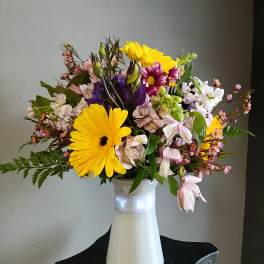Mixed bouquet of yellow daisies, pink and purple blooms in a white vase