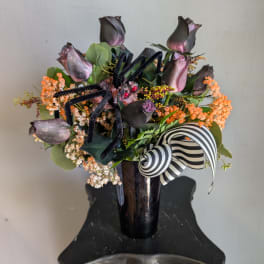 Dark roses in a black vase with orange filler and a striped ribbon.