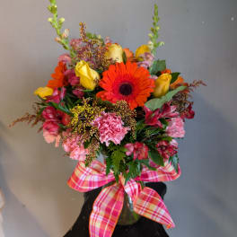 Bright mixed bouquet in a glass vase with a plaid ribbon bow