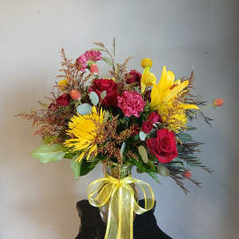 Bouquet of red roses, yellow lilies, and pink carnations in a glass vase with a yellow ribbon