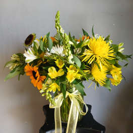 Mixed yellow, white, and orange flowers arranged in a glass vase with a ribbon