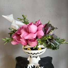 Pink roses arranged in a white Halloween-style vase with green foliage
