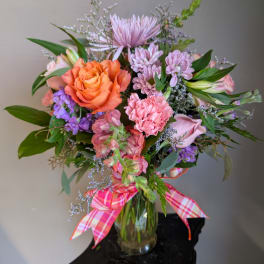 Mixed bouquet of orange, pink, and purple flowers in a glass vase with a plaid ribbon