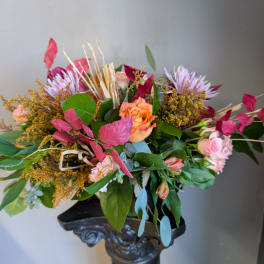 Mixed bouquet with peach roses, pink blooms, and purple flowers in a dark vase