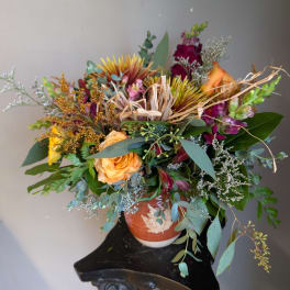Mixed bouquet of orange, purple, and yellow flowers in a terracotta vase