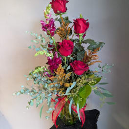 Tall bouquet of red roses and purple flowers in a glass vase with a red ribbon