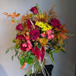Bouquet of red roses, pink spray roses, and yellow mums in a glass vase