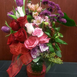 Bouquet of roses, tulips, and purple flowers in a pink glass vase