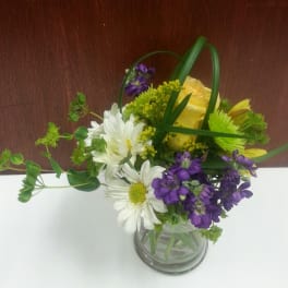 Bouquet of white daisies, yellow roses, and purple flowers in a glass vase