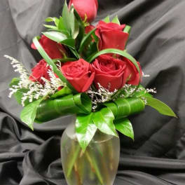 Red roses arranged in a glass vase with green ribbon accents