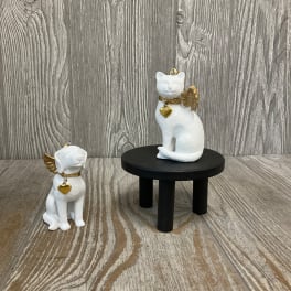 Two white cat figurines with gold wings and heart charms on a wooden surface