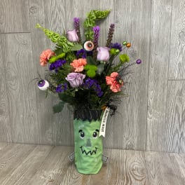 Halloween bouquet in a Frankenstein-themed vase with purple and orange flowers