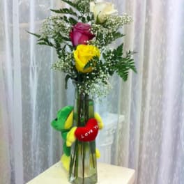 Tall bouquet of roses in a glass vase with a plush frog and heart