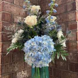 Blue hydrangea and white rose arrangement in a teal glass vase