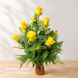 Yellow roses arranged in a brown glass vase with lush greenery